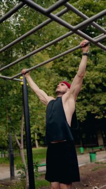Kararlı bir erkek sporcu, bir park ortamındaki yatay bir çubukta barfiks çeker. Formda kalmaya olan bağlılığını ve gücünü gösterir. Yeşiller yemyeşil bir ortam yaratıyor. Odaklandıkça sakin bir atmosfer yaratıyor.