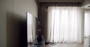 Gösterişli bir televizyonu, şık bir lambası ve doğal ışığı dağıtan uzun, şeffaf perdeleri olan sakin bir oturma odası..