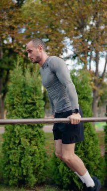 Parktaki paralel barlara dalan bir adam fitness ve güç eğitimine olan bağlılığını sergiliyor. Antrenman kıyafeti giyiyor ve ilerlemesini izlemek için bir fitness takip cihazı kullanıyor..