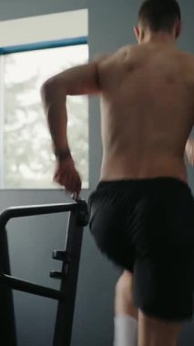 İyi donanımlı bir spor salonundaki koşu bandında koşan odaklanmış genç bir adam. Formunu ve sağlıklı yaşam tarzını ön plana çıkarıyor. Modern bir spor salonunda koşu bandında koşan genç adam. Dikey video.