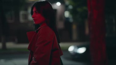 Şehir ortamında kırmızı ışıkta duran kendine güvenen gizemli bir kadın. Gece arkaplanı ve dramatik ışıklandırma entrika ve zarafet hissi yaratıyor. Kırmızı Işıklı Kadın