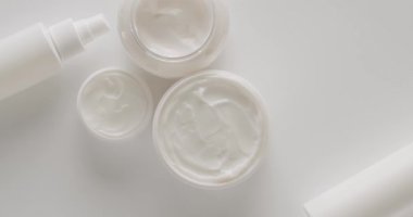 Beyaz kavanozlar ve kozmetik tüpleri stüdyoda beyaz bir arka planda dönüyor. Doğal malzemelere dayalı kozmetik yağları, fırça, serum, tonik, vücut bakımı, cilt bakımı. Kremalı parlak kozmetik kavanozu.