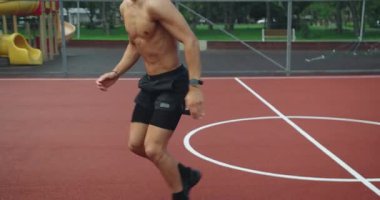 Atletik adam dışarıda antrenman yapıyor ve spor sahasında zıplayarak ve iterek burpee egzersizi yapıyor. Kaslı vücutlu genç bir erkek dışarıda yoğun bir fiziksel eğitime sahip. Açık hava Fitness Parkı.