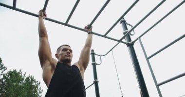 Genç atletik adam dışarıda egzersiz yapıyor ve yatay çubuğa yanaşıyor. Sportif adam spor alanında antrenman yapıyor, kol ve vücut kaslarını çalıştırıyor. Atletik adam dışarıda antrenman yapıyor..