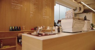 İçinde espresso makinesi, düzenli kahve fincanları ve içki menüsünün net bir görüntüsü olan iyi ışıklandırılmış modern bir kahve dükkanı. Ahşap estetik sıcaklık katıyor..