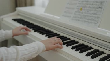 Genç kız evde piyano çalışıyor. Eğitim ve öğrenim geliştirme konsepti. Odaklanmış genç, güzel bir kız. Elektrikli piyano çalarak eğleniyor. Eller piyano tuşlarına basıyor. Nota okunuyor.