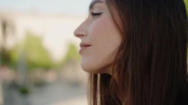 Uzun saçlı, gözleri kapalı, açık havada olan sakin genç bir kadının yakın plan profili. Arka plan, sükunet ve huzuru vurgulayan, yumuşak, bulanık bir doğal ortam. Profil Portresi Kadını