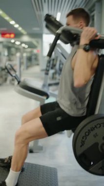 Azimli Genç Adam Spor Salonundaki Bacak Basın Makinesi 'nde çalışıyor. Modern bir spor salonunda ayak presi yapan odaklanmış genç bir erkek atlet. Göstergeler fitness, kuvvet, dikey video.