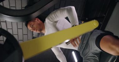 Modern bir spor salonunda bacak pres makinesi kullanarak spor kıyafetlerine odaklanmış genç bir erkek. Bu görüntü fitness eğitiminde kendini adamanın ve gücün özünü yakalar. Bacak Bastırma Makinesi 'ndeki genç adam. Dikey