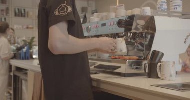 Moda bir kafede odaklanmış bir barista endüstriyel ekipmanlarla kahve yaparken görülüyor. Arka planda müşteriler ve diğer personel görülebilir, Chisinau - Moldova. 27 Temmuz 2023