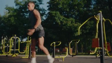 Parkta çalışan kaslı bir adam, dışarıda egzersiz yapıyor. Güneşli bir günde parktaki spor aletlerini kullanıyor. Güç ve özveri gösterisi yapıyor. Formda Adam Parkta Dışarıda Egzersiz Yapıyor