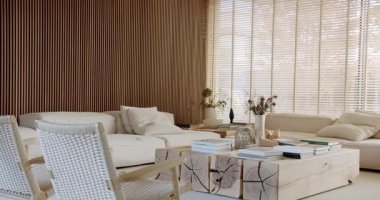 Özel bir sehpa, büyük bir kanepe ve koltuklar da dahil olmak üzere ahşap mobilyaları olan rahat ve şık bir oturma odası. Doğal ışık panjurların arasından süzülerek sıcak ve davetkar bir atmosfer yaratır..