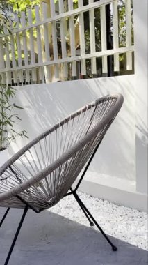 Güneşli bir verandada şık bir Acapulco sandalyesi olan rahatlatıcı bir açık hava sahnesi. Beyaz çakıl taşları minimalist tasarıma biraz zen katıyor. Yaşam tarzı, seyahat veya ev dekoru içeriği için ideal.