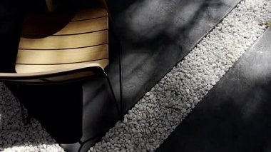 Beyaz çakıl taşları ve koyu betonu olan modern bir avluda tahta sandalye. Güneş ışığı ve gölgeler barışçıl bir atmosfer yaratır. Açık mobilya, rahatlama ve çağdaş tasarım ile ilgili projeler.