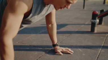 Açık havada şınav çeken kararlı bir genç adam, dayanıklılık ve fiziksel kondisyon gösteriyor. Güneş sıcak bir ışık saçıyor, atletik kararlılığı vurguluyor..