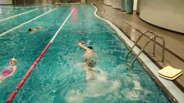 Kapalı havuzda aktif yüzücüler, Lanes egzersizlerle meşgul. Kapalı bir yüzme havuzu, yüzme gözlüğü ve yüzme şapkası takan aktivite yüzücüleriyle dolu. Hepsi de kucak yüzme yarışlarına katılıyor..