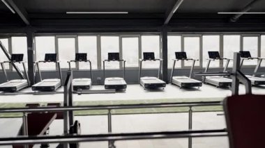 Geniş pencerelere bakan yüksek kaliteli koşu bantlarıyla donatılmış el değmemiş modern bir spor salonu, egzersiz yaparken kentsel bir manzara sunuyor. Şehre Bakışlı Çoklu Koşu Değirmenleriyle Modern Spor Salonu