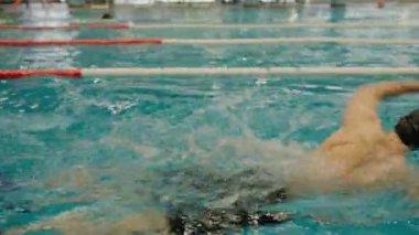 Odaklanmış bir yüzücü, kapalı havuzda serbest yüzerken dinamik sıçramalar yaratarak hız ve güç gösterisi yapar. Kapalı Yüzme Havuzu 'nda Yarışma Yüzücüsü
