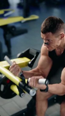 Kaslı bir adam vaiz bukle makinesinde biseps yapıyor. Spor salonunda ağırlık kaldırırken şekline ve nefes alışına odaklanıyor. Kendini spora ve dayanıklılık eğitimine adamış.