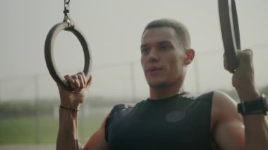 Açık hava parkında spor yapmak için jimnastik halkaları kullanan odaklanmış bir erkek sporcu. Kararlılığı ve uygunluğu yakalamak. Genç Adam Spor Salonu 'nda Jimnastik Yüzükleri Eğitimi