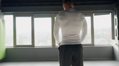 Formda, kaslı genç bir adam spor salonunda kendinden emin duruyor. Yoğun bakışları, güçlü fiziği, kendini adamışlığı ve gücü. Arkasından büyük pencerelerden gün ışığı akıyor..