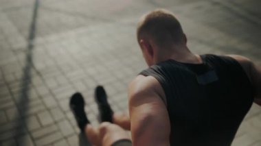 Odaklanmış genç erkek sporcu, şehir ortamında gün doğumundan önce, zihinsel ve fiziksel olarak hazırlanarak bacaklarını esnetiyor. Şehirde Sabah Koşusundan Önce Gerinen Atletik Adam