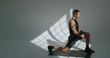 Atletik yapılı bir adam stüdyoda hamleler yapar, zindelik ve güç gösterisi yapar. Atletik Genç Adam Modern Stüdyo Ayarında Hamle Yapıyor