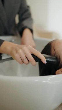 Bir müşteri kuaförde saçını yıkatıyor. Kuaför nazikçe kafa derisine masaj yapıp saçlarını duruluyor. Ürünlerin dağıtılmasını bile sağlıyorlar..