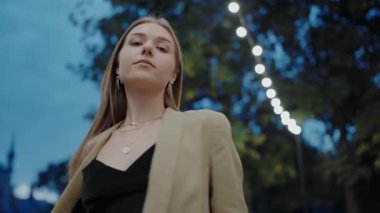 Portrait of a young woman with her hair flowing, captured on a dusky evening in an urban park. Focus on natural beauty and youthful elegance. Young Woman with Flowing Hair in Urban Evening Setting