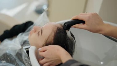 Genç bir kadın kuaförde saçını yıkarken rahatlıyor. Kuaför şampuanı durulurken nazikçe kafa derisine masaj yapıyor. Müşteri şımartılmaktan ve kendine bakmaktan zevk alır..