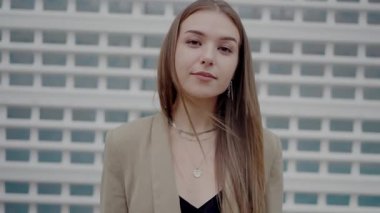 Portrait of a confident young female with a straight gaze, dressed in a chic outfit, standing against a geometrically patterned wall, embodying contemporary style and urban confidence.