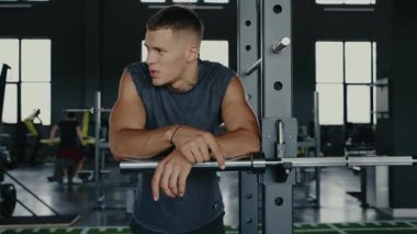 Genç adam modern bir spor salonunda çalışırken halterde dinleniyor, azim ve güç gösterisi yapıyor. Spor ve sağlık konsepti. Modern Spor Salonunda Güç Eğitiminde Odaklanan Genç Adam Mola Verdi