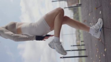 Beyaz giysili formda genç bir kadın güneşli bir günde, açık hava fitness parkında ters köşe yaparak esneklik ve güç gösterisi yapıyor. Fit Genç Kadın Outdoor 'da Backbend' i oynuyor. Dikey video.