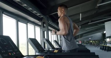 Geniş, iyi donanımlı bir spor salonunda koşu bandında koşan kararlı bir erkek atlet manzaralı bir manzaraya bakıyor, fitness bağlılığını sergiliyor. Modern bir spor salonunda koşu bandında koşan bir sporcu