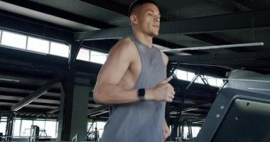 Formda bir genç adam, iyi donanımlı, ferah bir spor salonunda koşu bandında yoğun bir şekilde koşar. Formda kalma hedeflerine odaklanmış. Modern bir spor salonundaki koşu bandına odaklanmış genç adam.