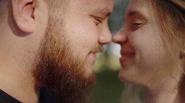 Genç bir erkek ve kadın, yumuşak, doğal bir ışıkla çerçevelenmiş olarak birbirlerinin gözlerine bakarken gülümseyerek yakın ve şefkatli bir anı paylaşırlar. Açık havada şefkatli bir anı paylaşan neşeli bir çiftin yakın çekimi