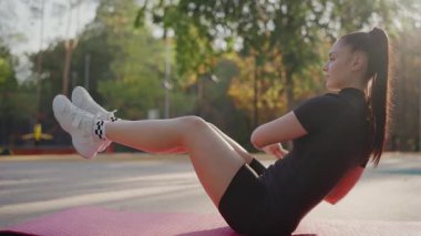 Odaklanmış genç bir kadın parkta pembe bir minder üzerinde karın egzersizleri yapıyor, güneşli bir açık hava fitness seansının tadını çıkarıyor. Genç Kadın Güneşli Gün 'de Açık Hava Spor Programına Girdi