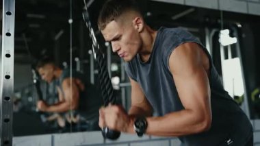 Modern bir spor salonunda güçlü ve kararlı bir şekilde triseps halatıyla çalışan bir adamın yakın çekimi. Modern Spor Salonu 'nda Triseps Halat Çekme Egzersizi Odaklanan Adam