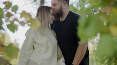Genç bir çift, zengin renkli yaprakların arasında mutluluk ve samimiyet saçan sonbahar arkaplanına sevgiyle sarılıyor. Romantik Sonbahar Gezintisi Parkta Kucaklaşan Genç Çift