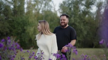 Genç bir çift, birlikte huzurlu ve sevgi dolu bir anı paylaşan mor çiçeklerle dolu canlı bir tarlada yürüyor. Aşk, ilişkiler ve doğa temaları için mükemmel..