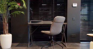 Rahat çalışma odasında minimalist deri koltuklu modern ahşap çalışma masası. Oda palmiyesi dekoru. Minimalist siyah panjurlar. Beauty Interior 'da yatak odası aksesuarı, deri koltuk ve modern masa..