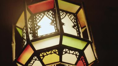 Karmaşık, renkli bir Fas fenerinin yakın çekimi. Ilık ışık desenli camların arasından parlayarak büyüleyici bir ortam yaratır. egzotik kültür ve huzurlu geceler.