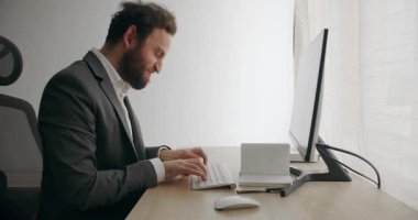 Evde çalışan gri takım elbiseli kızgın bir iş adamı. Şimdiki yaşam tarzı ve iletişim teknolojisi kullanılarak çalışma. Gri takım elbiseli agresif adam evde online çalışarak bilgisayar kullanıyor..