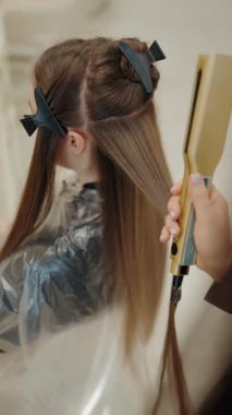 Bir kuaför, müşterilerini ustalıkla düzeltir. Uzun kahverengi saçlı, düz ütülü, profesyonel bir kuaför salonu ortamında. Kuaför saçı dikkatlice kesiyor ve kesiyor, pürüzsüz ve pürüzsüz bir şekilde bitiriyor..