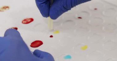 Crop doctor mixing blood with chemicals. From above closeup handheld shot of anonymous medical specialist in latex gloves mixing blood samples with reagents during work in clinic lab.