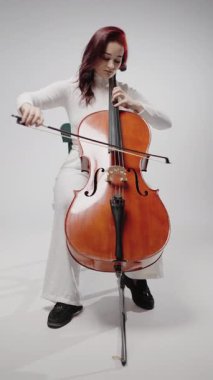 Stüdyoda beyaz arka planda çello çalan güzel bir kadın. Klasik müzik yaylı klasik müzik enstrümanları, kadın çellocu solo parça çalışıyor.