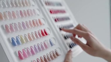 Bir kadının eli bir güzellik salonundaki paletten oje rengini seçiyor. Çeşitli gölgeler gösterildi. Renkli oje örnekleri. Güzellik Salonundan Tırnak Cilalama Rengi Seçen Kadın