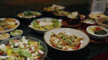 Açık büfe masasında çeşitli rengarenk salatalar ve Akdeniz yemekleri, sağlıklı bir yemek için mükemmel, canlı ve sağlıklı malzemeler sergileniyor. Renkli Taze Salatalar