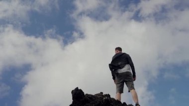 Sivri uçlu bir kaya oluşumunun tepesinde dikey duran bir adamın engin mavi gökyüzüne bakışını. Kararlılığı, keşfi ve yalnızlığı temsil eder. Rocky Dağının Tepesinde Duran Adam