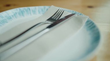 Peçetenin üzerine çatal ve bıçak yerleştirilmiş bir tabağın yakın plan görüntüsü yemek için zarif bir sofrayı işaret ediyor. Tabak üzerinde Çatal ve Bıçak ile Masa Ayarının Kapanışı